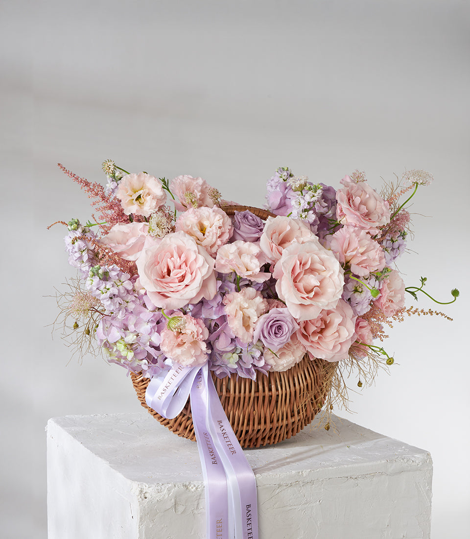 Blush pink roses with purple lisianthus in wicker basket arrangement