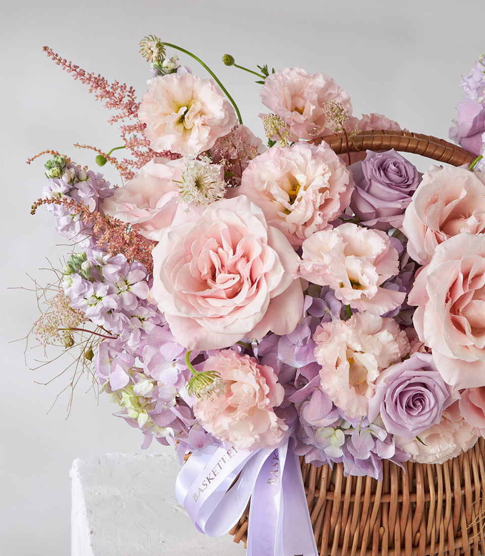 Blush pink roses and purple lisianthus in woven wicker basket with hydrangeas and accent flowers