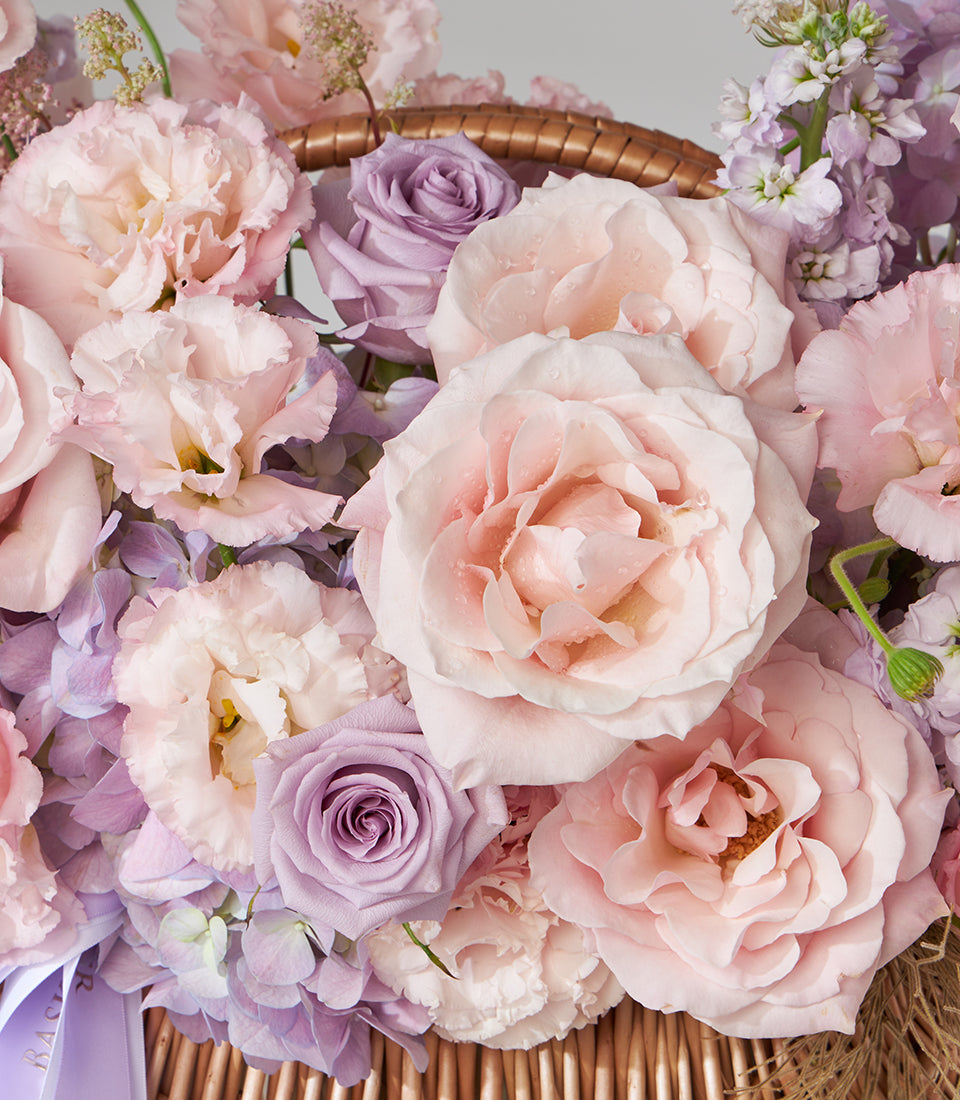 Blush pink roses and purple lisianthus arrangement in woven basket with hydrangea