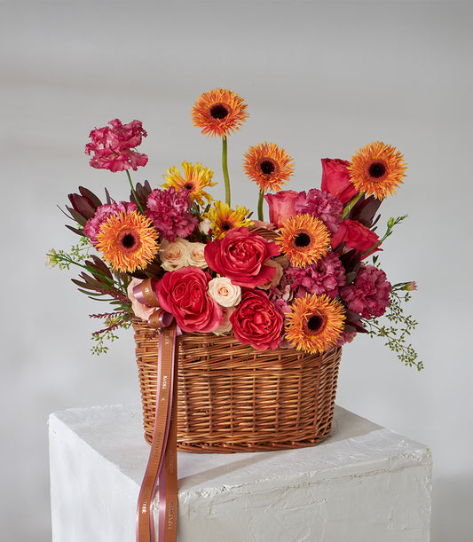 Red roses and orange gerbera daisies in woven wicker gift basket with ribbon