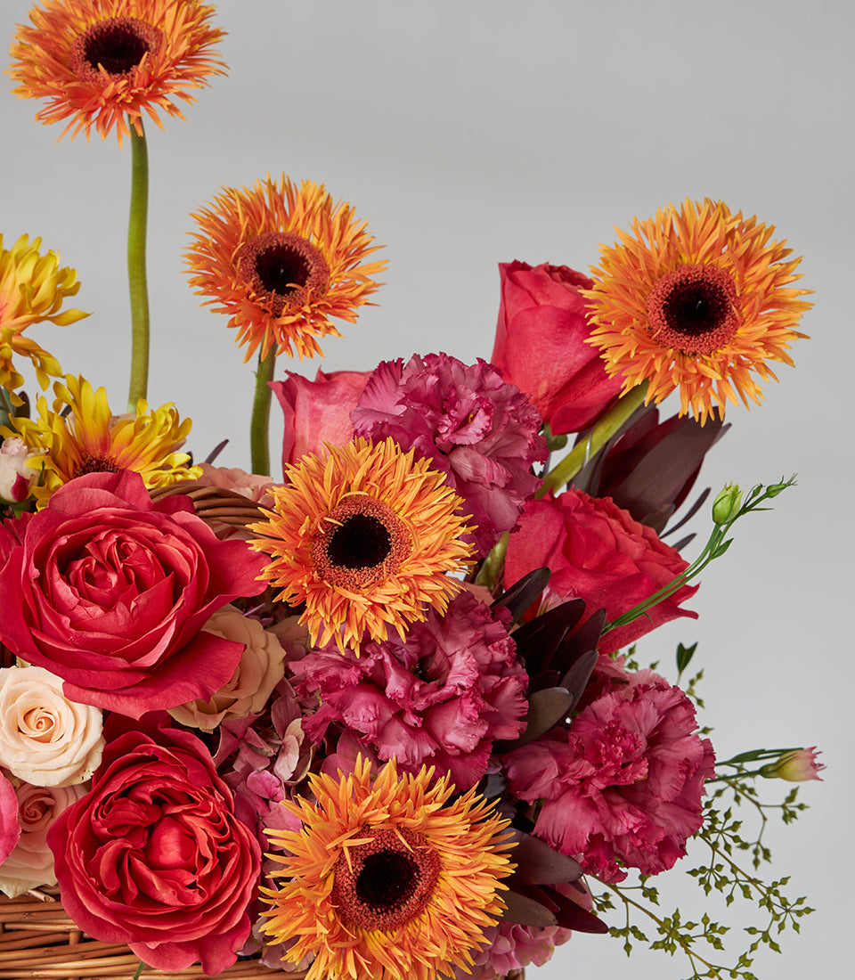 Red roses and orange gerbera daisies in woven basket with warm-toned blooms