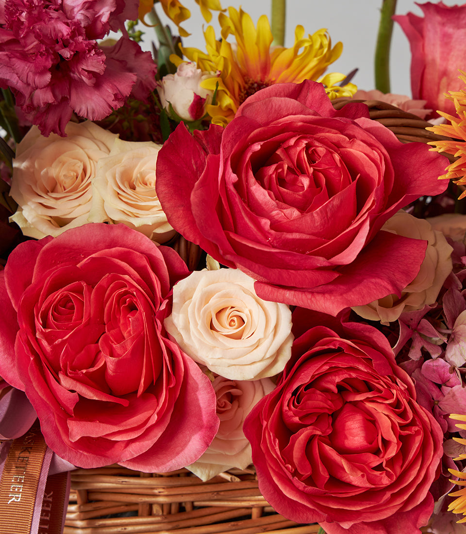 Vibrant red roses and orange gerbera in woven basket with cream and deep pink blooms