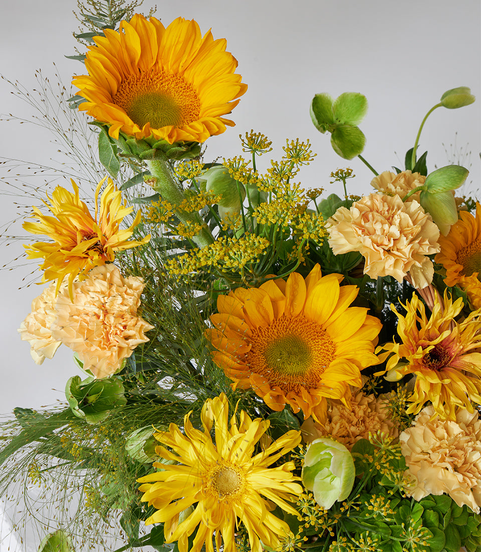 Vibrant yellow sunflowers, carnations and chrysanthemums in a woven basket arrangement