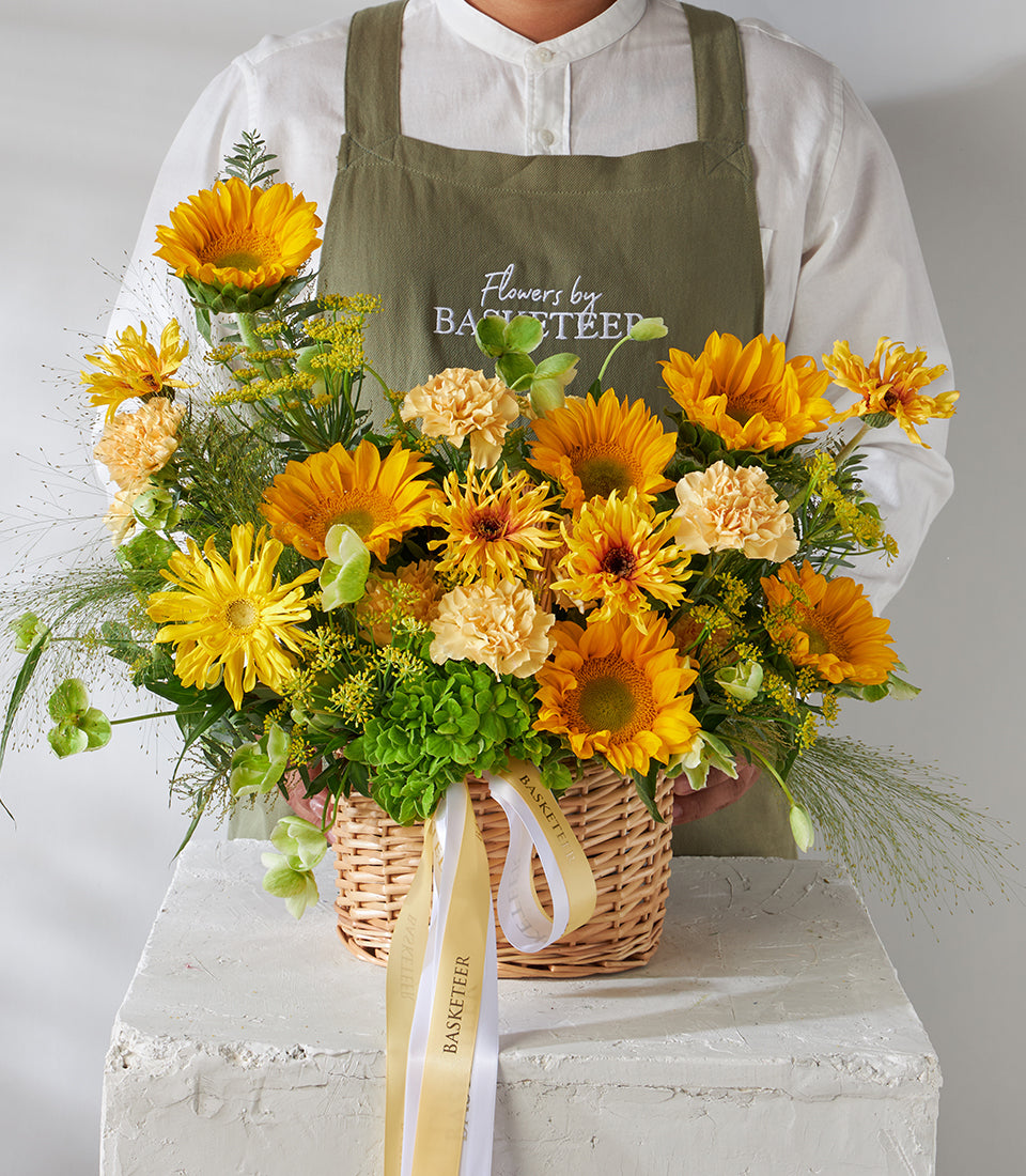 Vibrant yellow sunflower and carnation bouquet in woven basket with gold ribbon