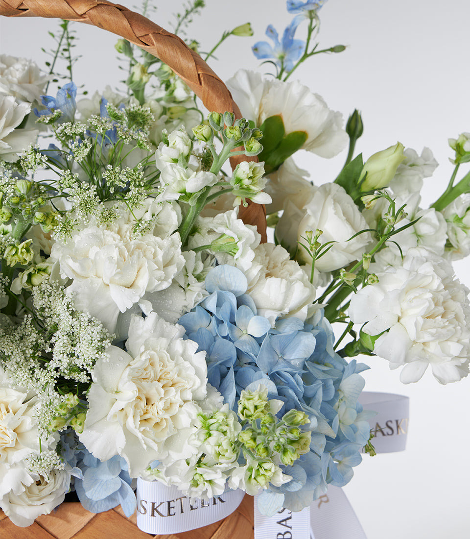 White carnations and blue hydrangeas in woven basket with fresh flower filler