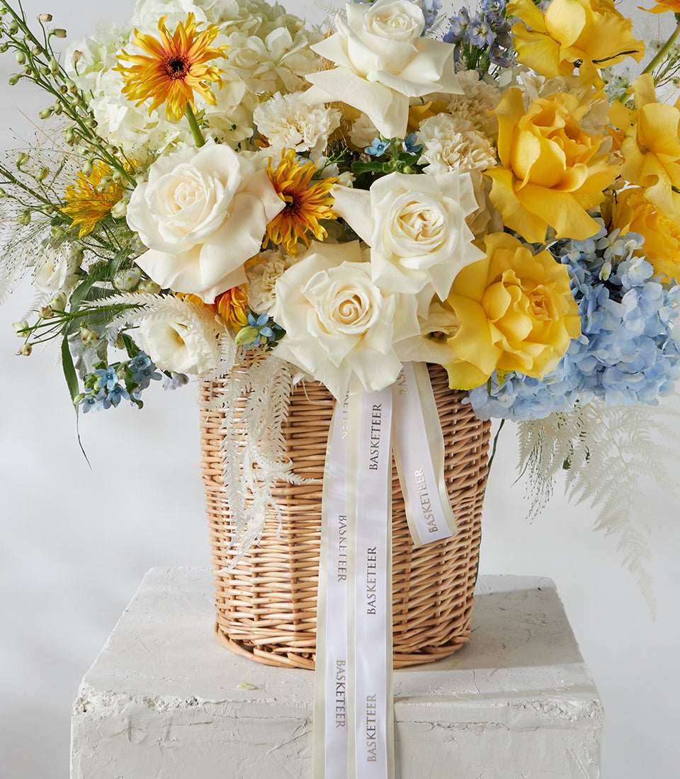 White and yellow roses with blue hydrangeas in woven wicker basket
