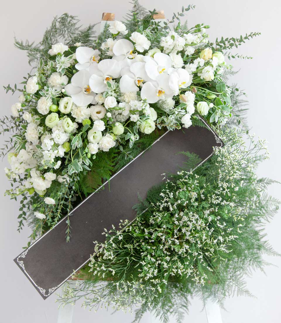 White orchid and carnation funeral wreath with green foliage and sympathy ribbon