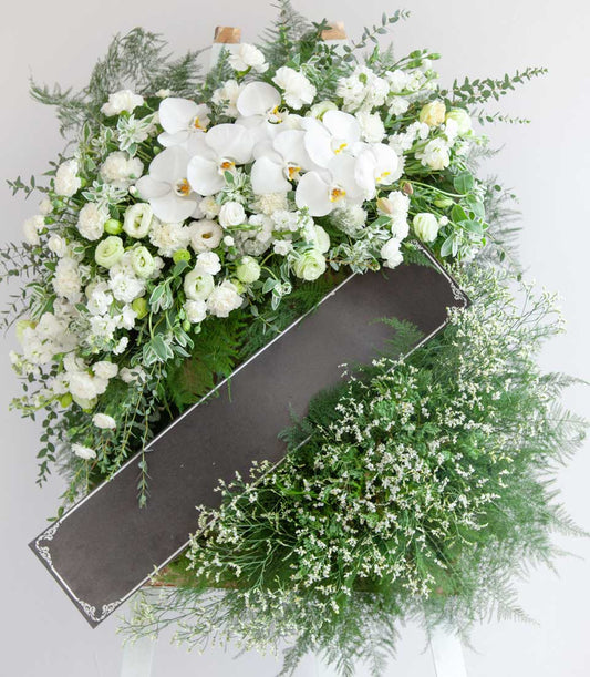 White orchid and carnation funeral wreath with green foliage and sympathy ribbon