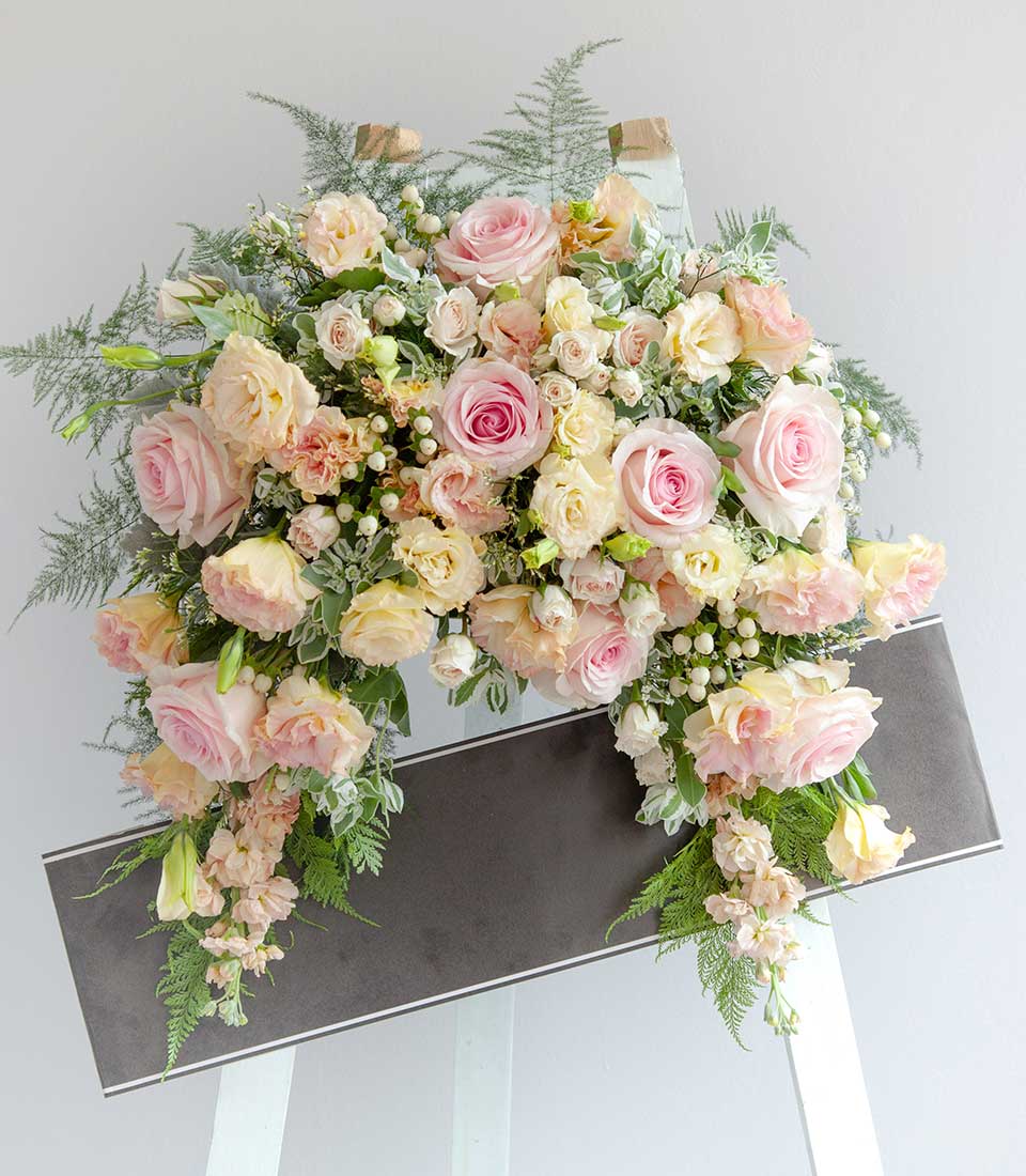 Comforting Farewell Wreath with blush roses, cream blooms, and cascading greenery on sympathy easel