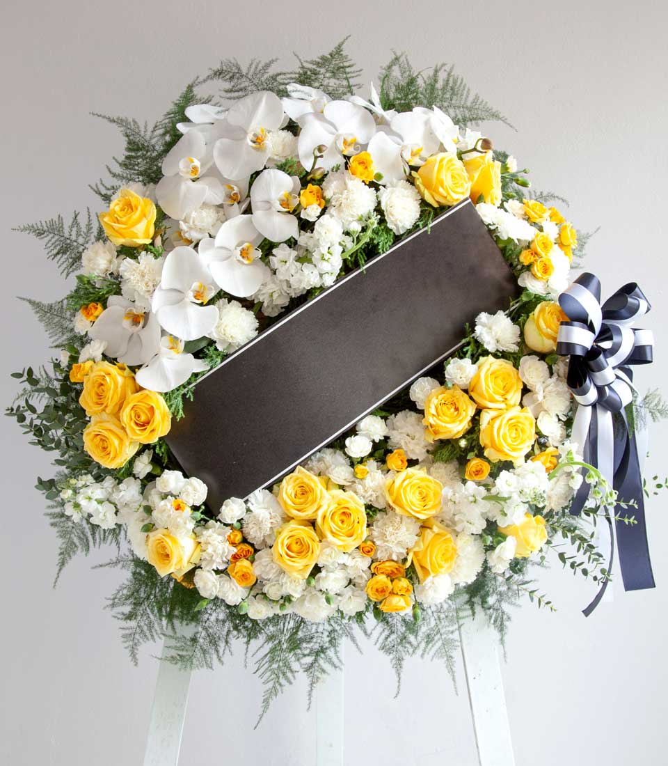 Eternal Sunshine orchid wreath with yellow roses, white orchids, and black ribbon on easel for memorial tributes