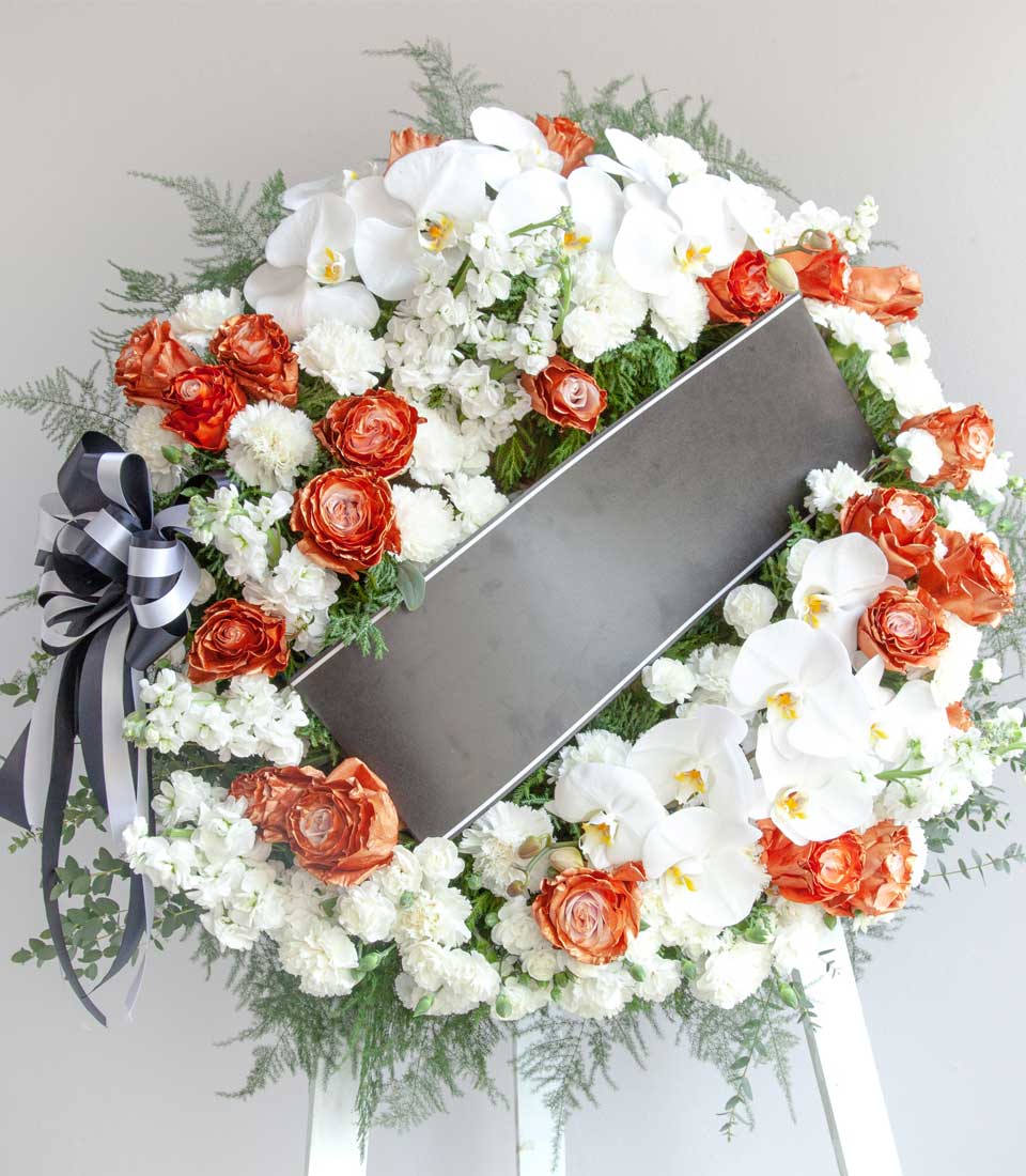 Elegant floral wreath from Flowers by Basketeer features white orchids, delicate white blooms and striking orange roses, a beautiful tribute for flower delivery in Bangkok.