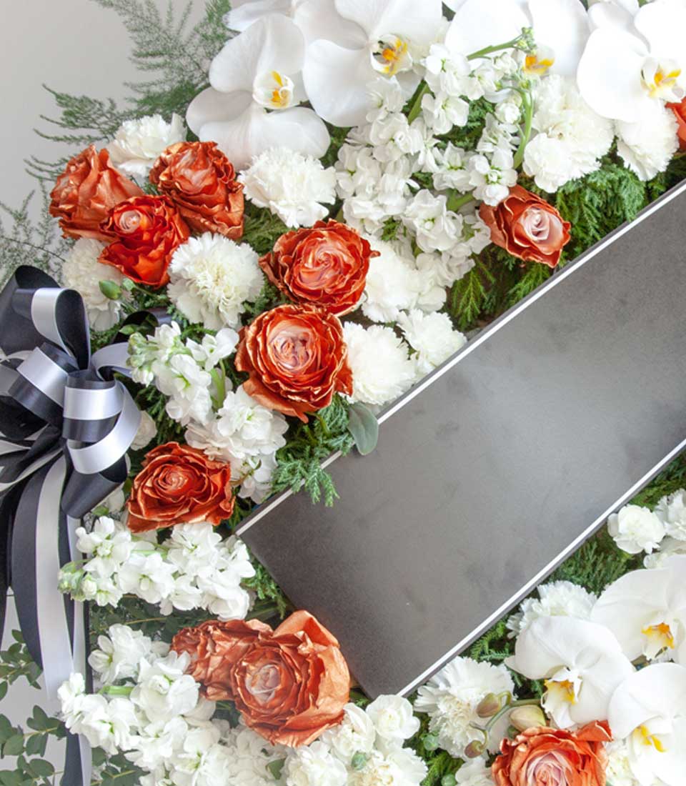 Elegant Flowers by Basketeer tribute wreath. Featuring orange roses, white orchids and carnations, plus lush greenery. A premium flower delivery Bangkok choice.