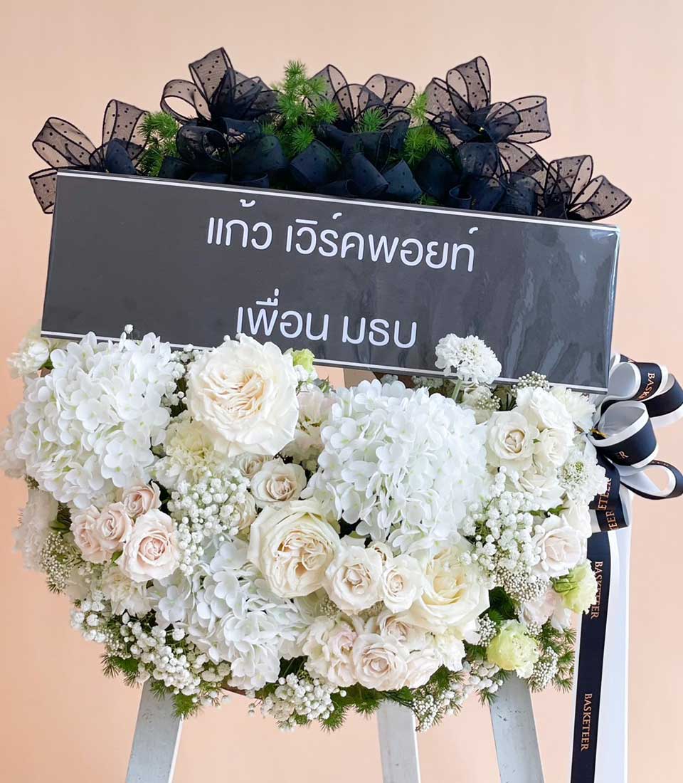 Elegant white funeral wreath with hydrangeas, roses, and baby's breath on easel stand