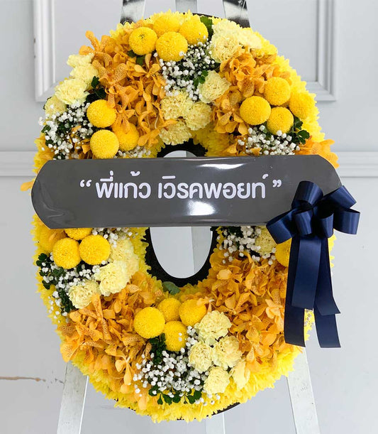 Yellow and orange floral wreath with chrysanthemums, carnations, orchids, and baby's breath on white easel