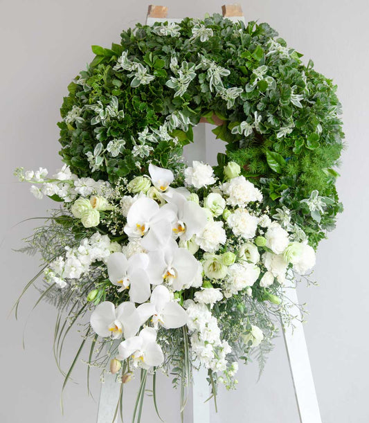 Serene Farewell Petals Wreath with white orchids, carnations, and lush green foliage sympathy arrangement