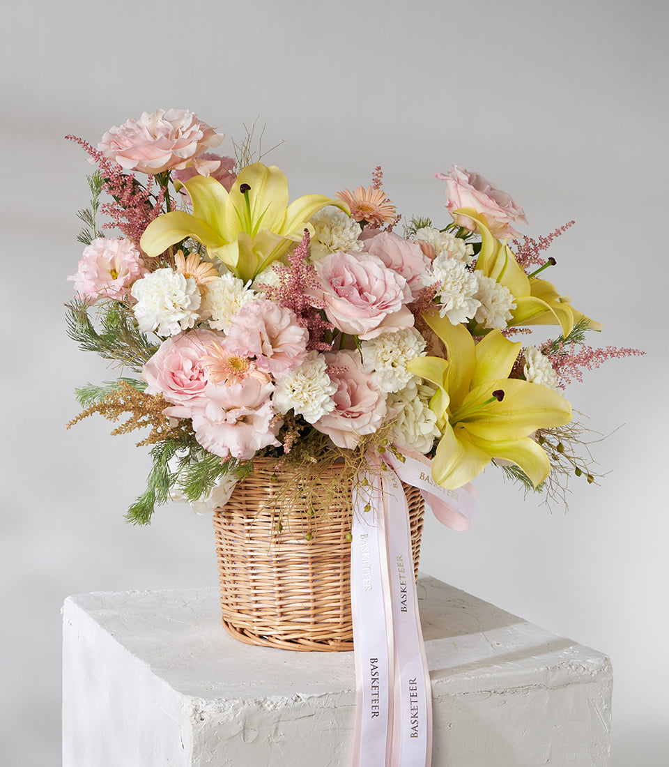 Yellow lilies and pink roses in woven basket with white carnations and astilbe