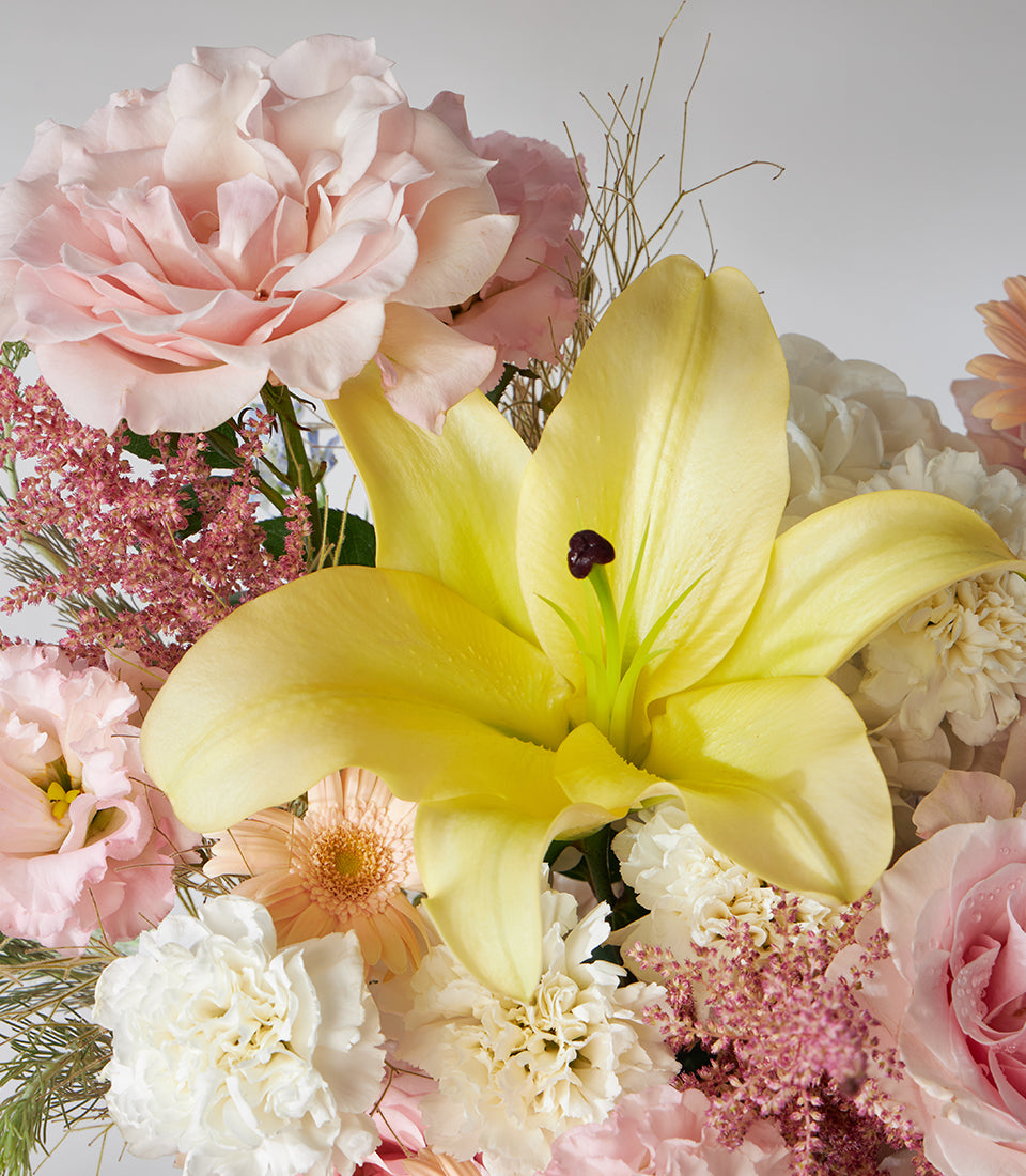 Vibrant yellow lily and pink roses in a lush basket arrangement with astilbe and carnations