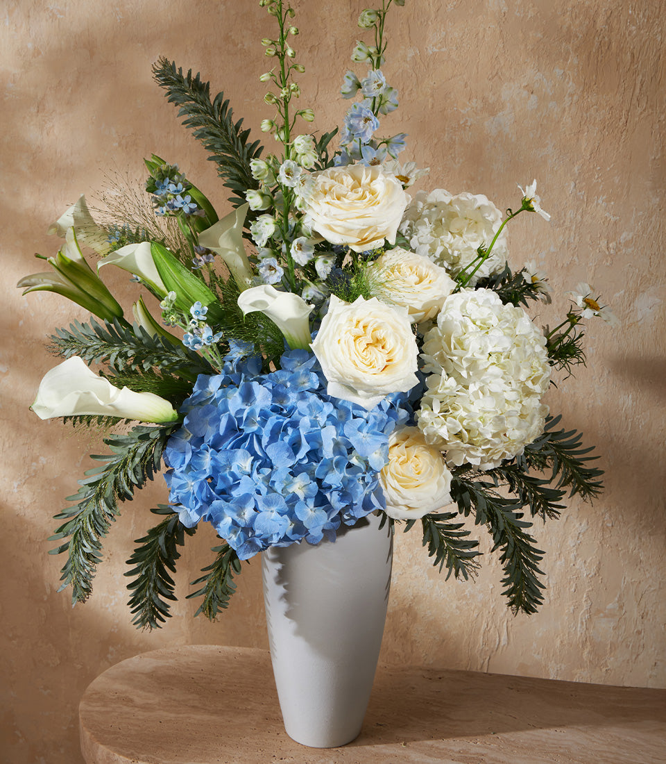 Elegant white roses and blue hydrangea arrangement in tall gray ceramic vase