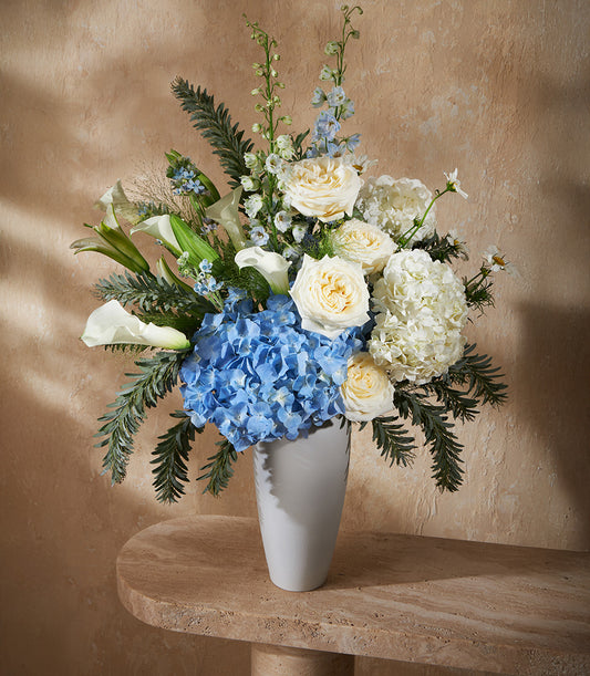 Tall grey ceramic vase with blue hydrangeas, white roses and calla lilies, fresh flower arrangement
