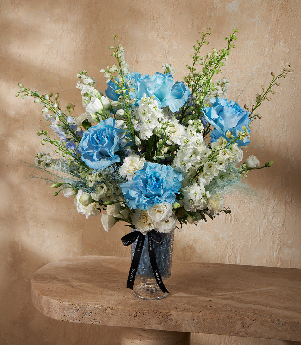 Elegant blue and white rose arrangement in textured glass vase with stock and delphinium flowers