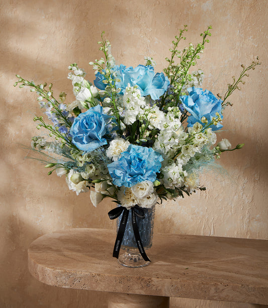 Elegant blue and white rose arrangement in textured glass vase with stock and delphinium flowers
