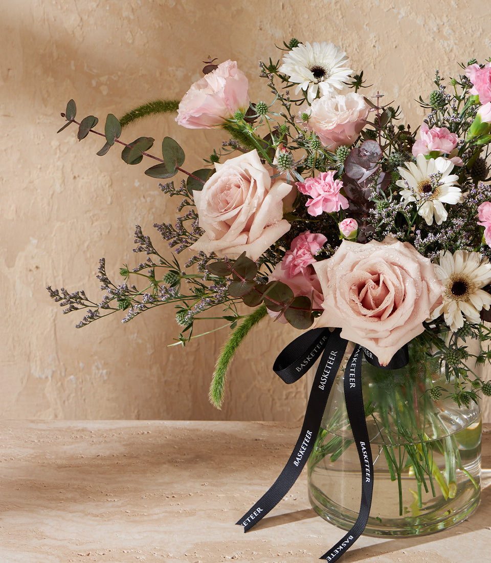 Fresh pink roses and white gerbera daisies in clear glass vase with green foliage
