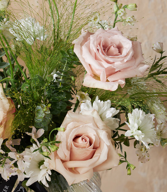 Light pink roses and white flowers in elegant clear ribbed glass vase with fresh greenery