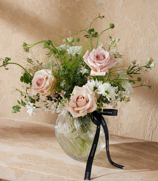 Elegant light pink roses and white chrysanthemums in a clear ribbed glass vase with green foliage