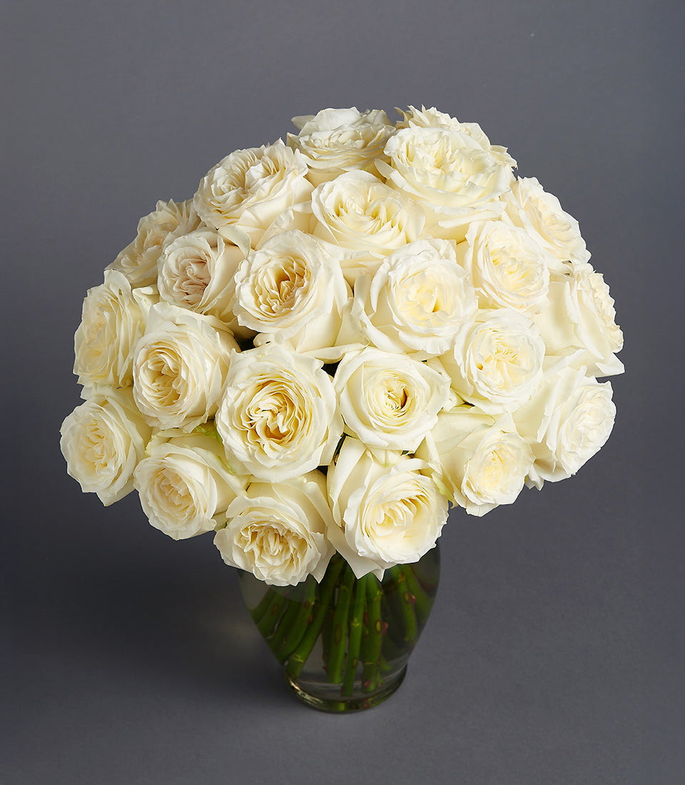 Creamy white roses in rounded dome arrangement within clear glass vase, luxury fresh flower gift