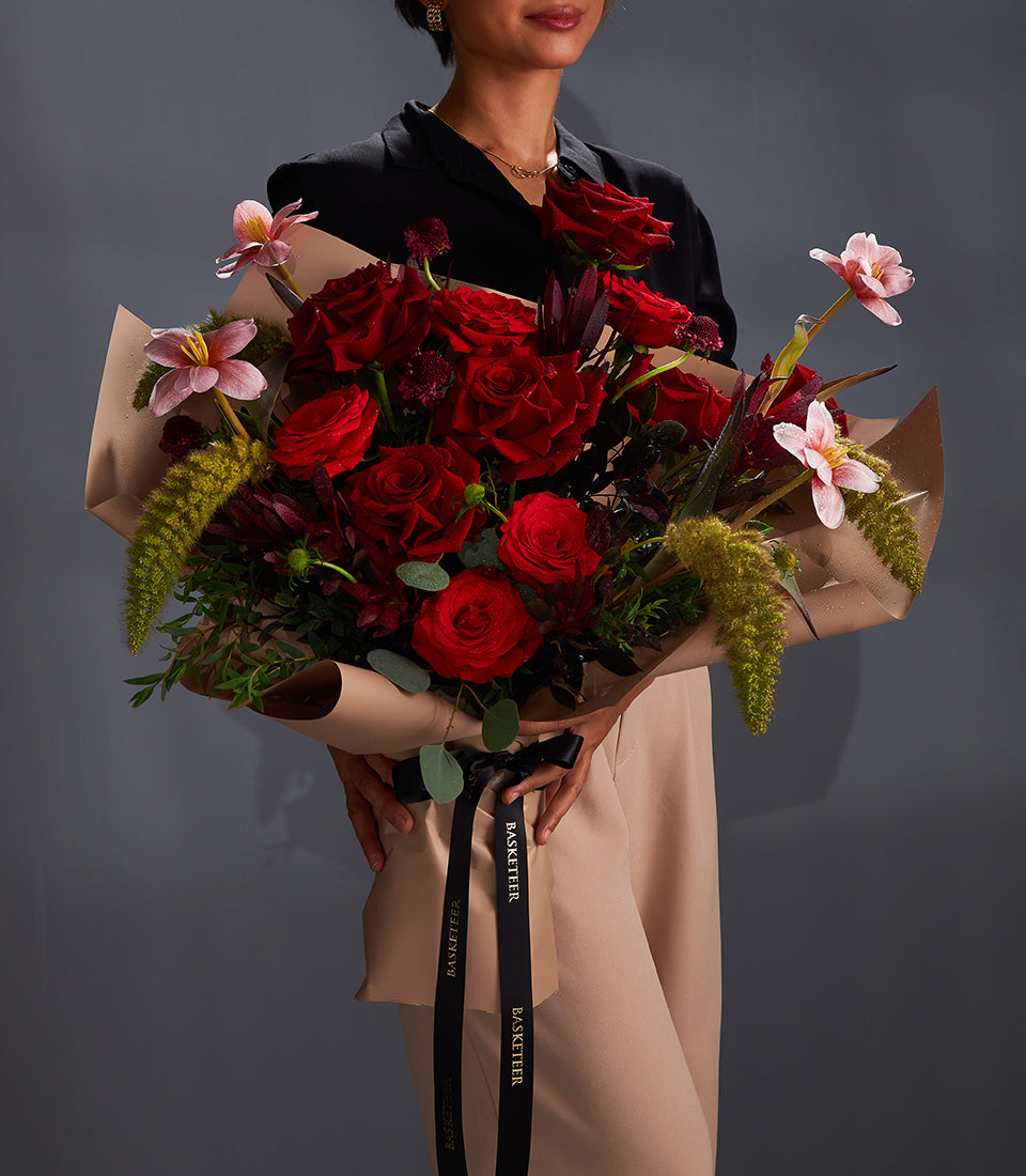 Large bouquet of deep red Ecuador roses with burgundy accents, pink star flowers, and feathery green foliage, wrapped in
