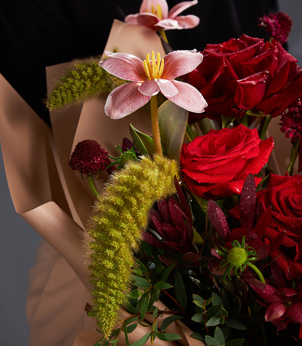 Red roses and pink lilies with burgundy accents in fresh wrapped bouquet for gifting