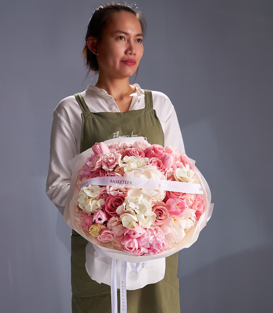 Florist holding blush peony and rose bouquet with white hydrangeas and ribbon