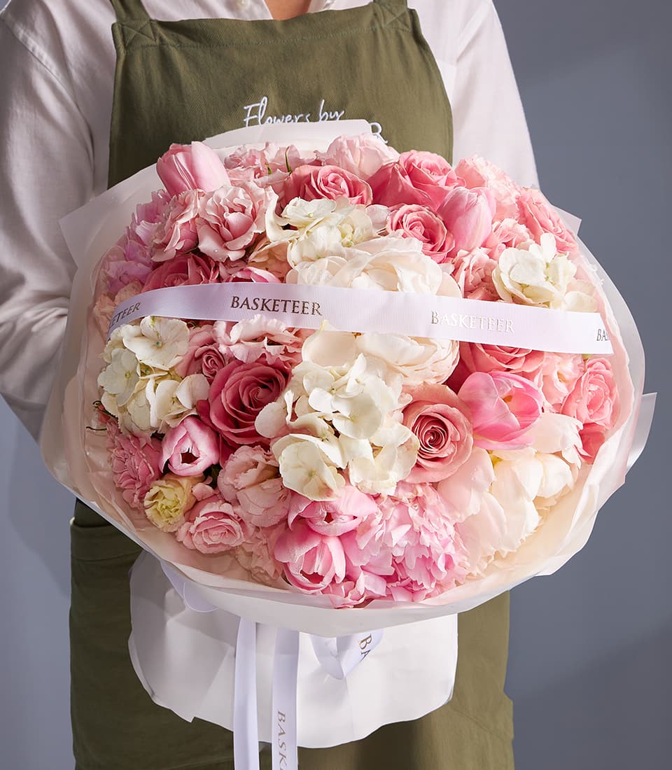 Florist holding lush blush and white peony rose hydrangea bouquet wrapped in pink paper with white ribbons