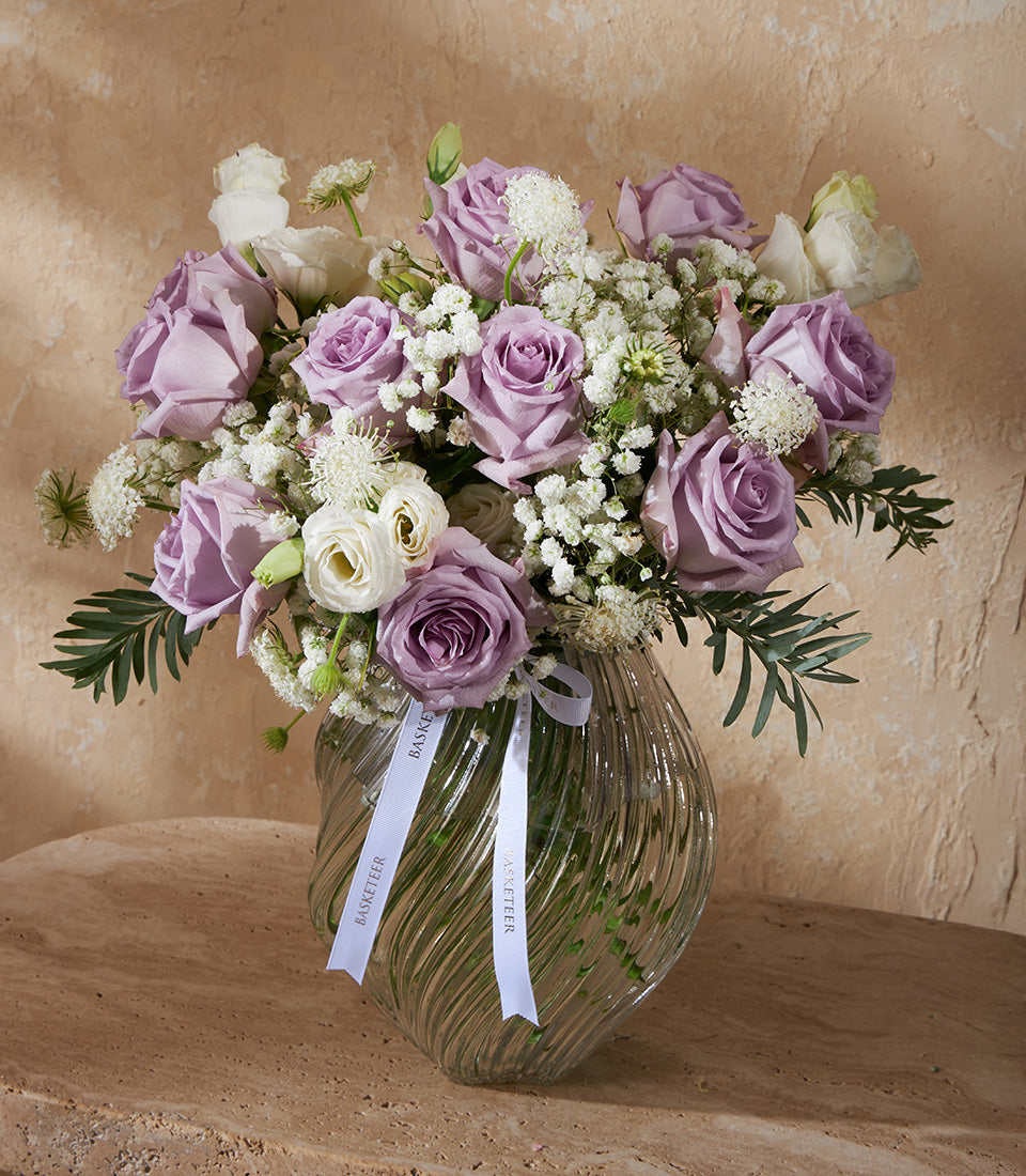 Lavender and white rose bouquet in ribbed glass vase with baby's breath and ranunculus
