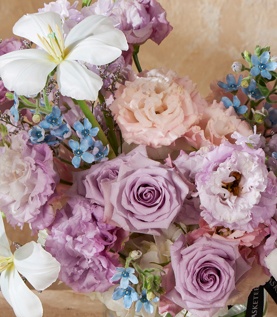 Ethereal lavender vase arrangement with white clematis, pink lisianthus, and forget-me-nots in soft pastels