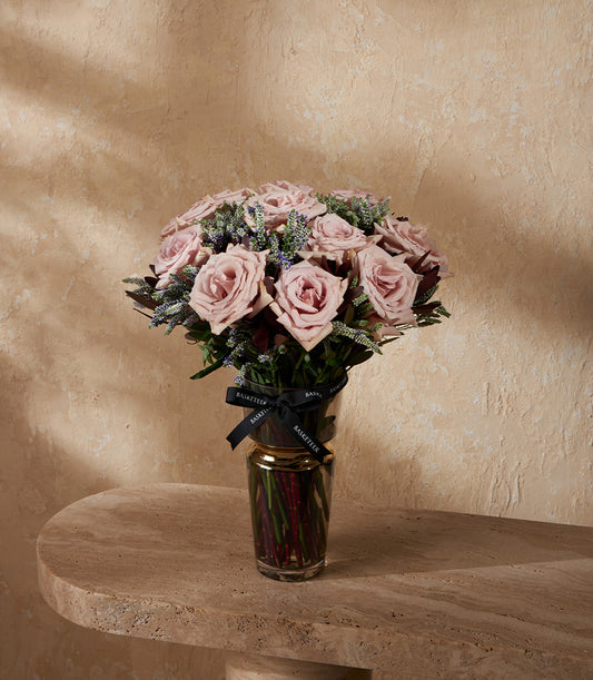 Light pink roses and purple filler flowers in clear glass vase with gold rim, black ribbon detail