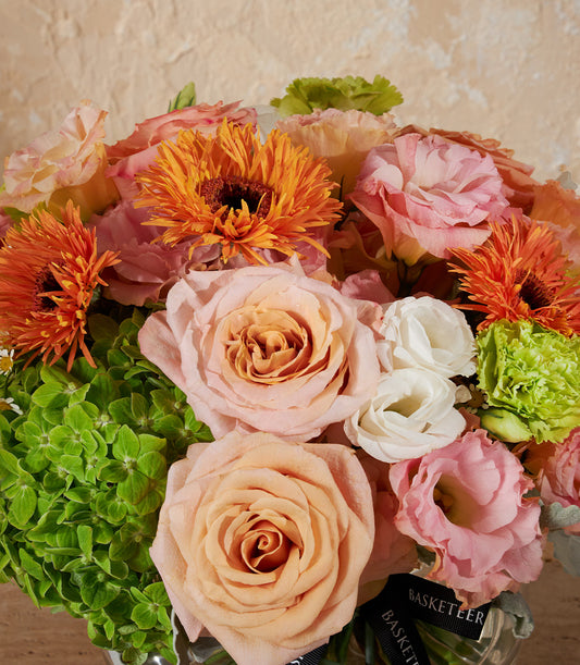 Radiant peach and pink rose arrangement with gerbera daisies and lisianthus in clear glass vase