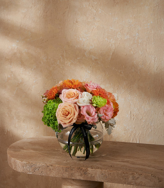 Radiant Harmony vase arrangement with orange roses, peach dahlias, pink hydrangeas, and white flowers in clear spherical