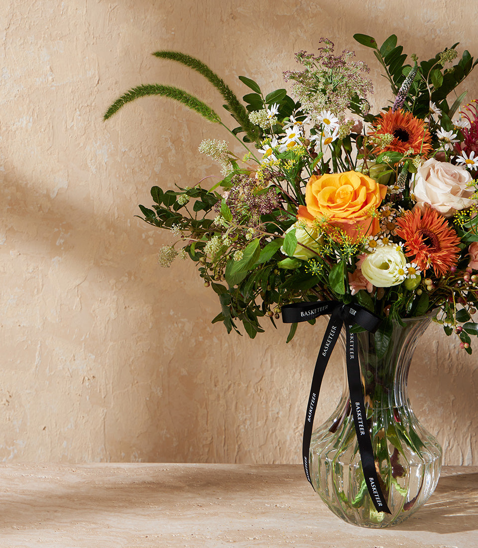 Vibrant orange roses and gerbera daisies with pink roses in clear glass vase arrangement
