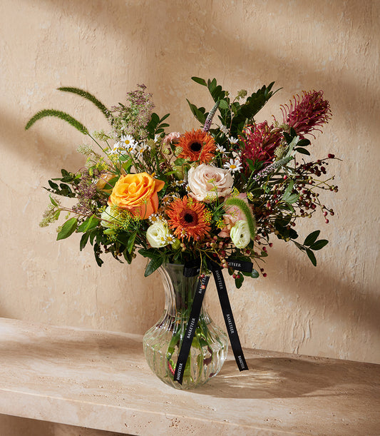 Vibrant mixed flower arrangement with orange roses, peach gerberas, and white ranunculus in ribbed glass vase