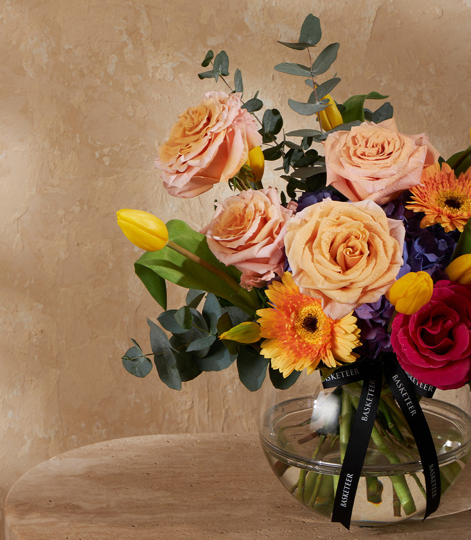 Peach and fuchsia rose arrangement with gerbera daisies, tulips, and hydrangea in clear glass vase