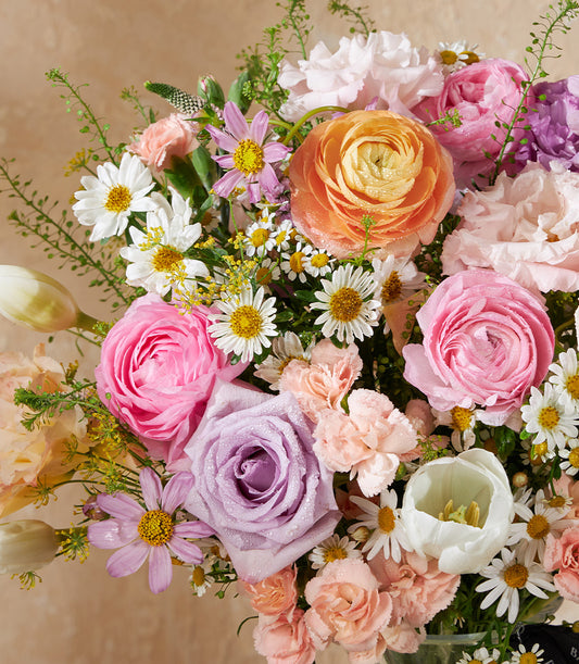 Pastel Bloom Symphony vase with fresh pink ranunculus, roses, tulips, and daisies in clear glass