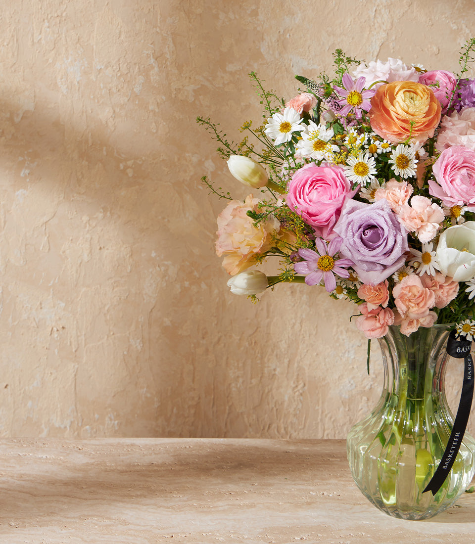Pastel Bloom Symphony fresh flower bouquet with roses, ranunculus, and tulips in pink, orange, and purple tones in clear