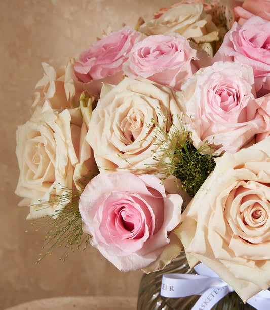 Fresh pink and cream roses with green foliage in ribbed glass vase, water droplets on petals