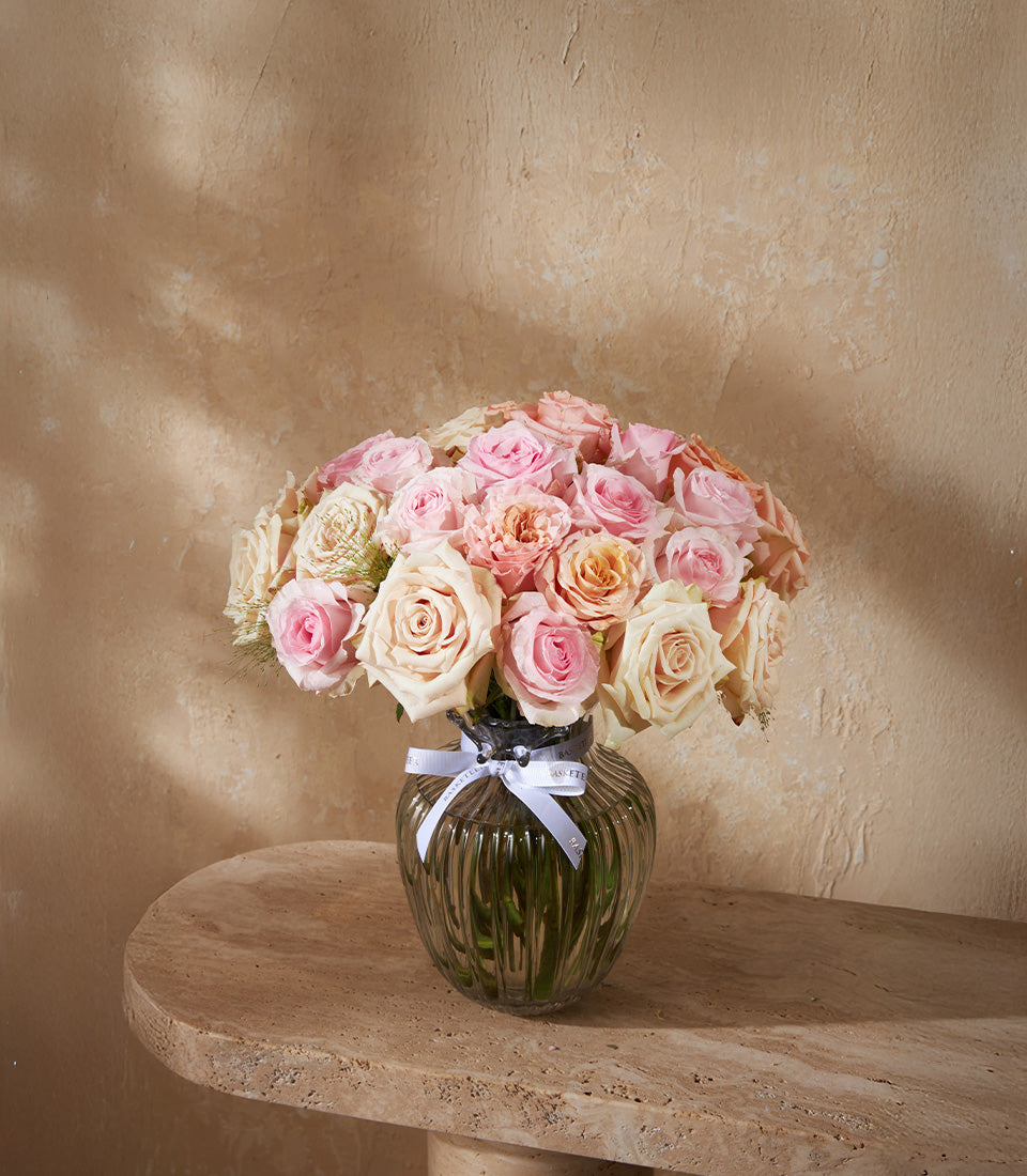 Light pink, peach and cream rose bouquet in ribbed glass vase with white ribbon