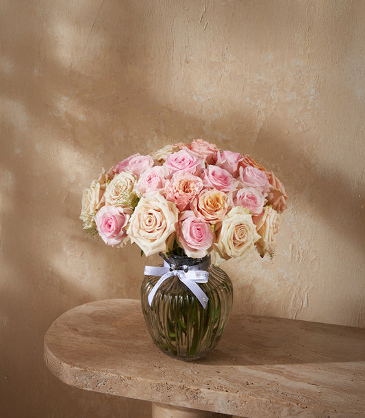 Light pink, peach and cream rose bouquet in ribbed glass vase with white ribbon