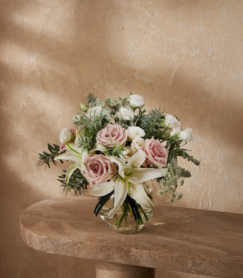 Premium white lilies and pink roses in glass vase with green foliage, luxury gift arrangement