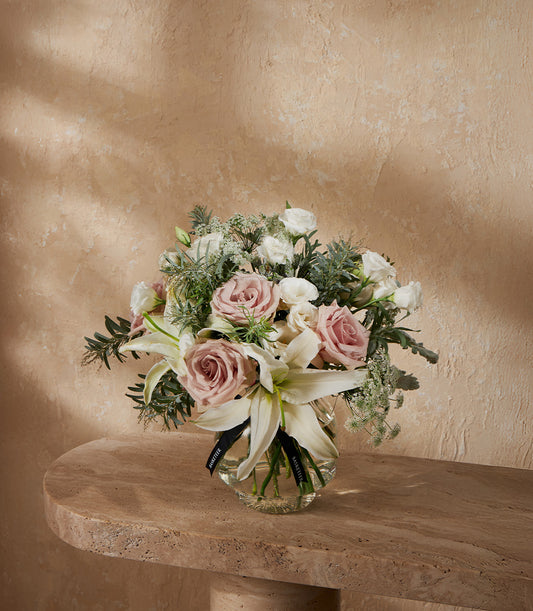 Premium white lilies and pink roses in glass vase with green foliage, luxury gift arrangement