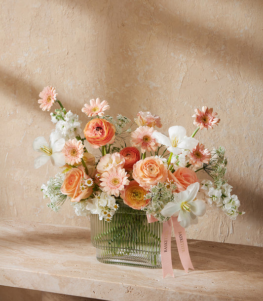 Peach and coral ranunculus roses arrangement in clear ribbed vase with pink ribbon