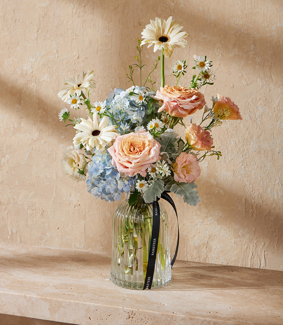 Radiant Harmony pastel floral vase arrangement with white gerberas, blue hydrangeas, and peach roses